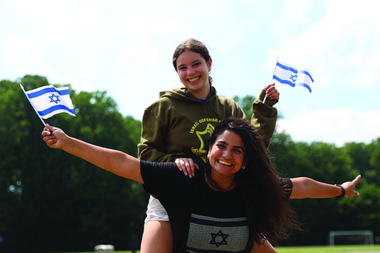 Maayan carries another camp staff member on her back and holds up an Israeli flag